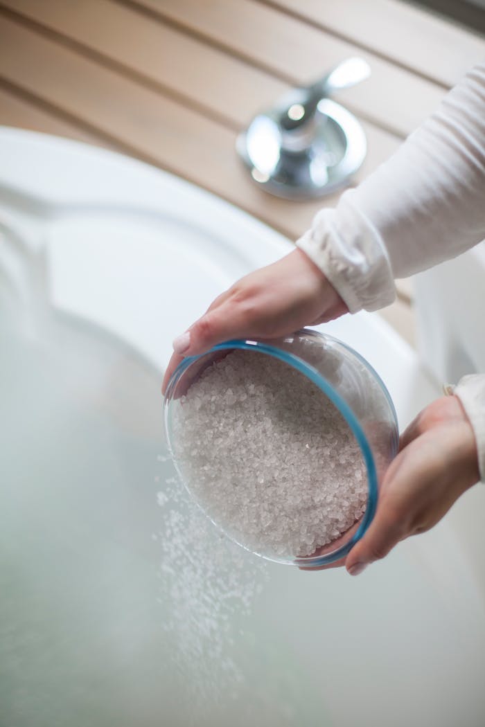 A woman pours bath salts into a jacuzzi, creating a luxurious and relaxing spa atmosphere.